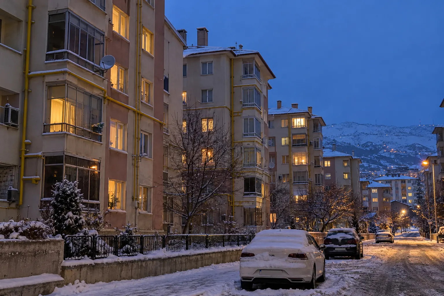 Kar yağmış bir kış akşamı, cephelerinde sarı doğalgaz boruları olan Elazığ apartmanları